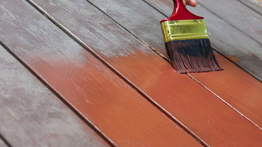 paint brush stroking wooden deck of pressure treated lumber