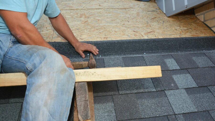 A man using a wooden plank to work on an OSB roof.