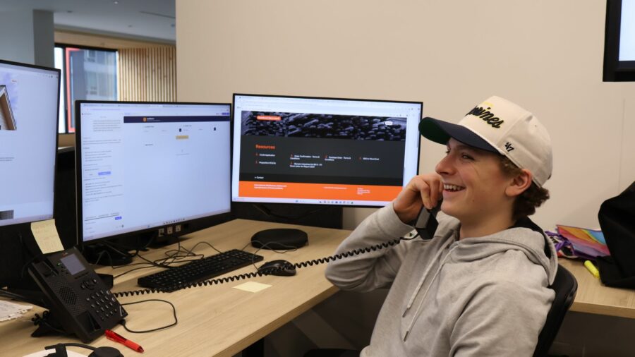 A young man sitting in front of a computer talking on the phone smiling