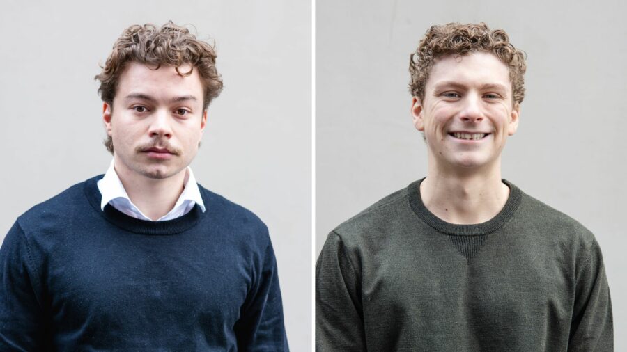 Two men infront of a grey wall smiling to the camera