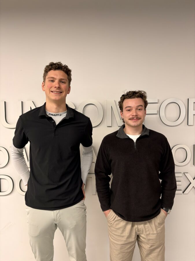 Two men smiling standing in front of a wall taking a group photo