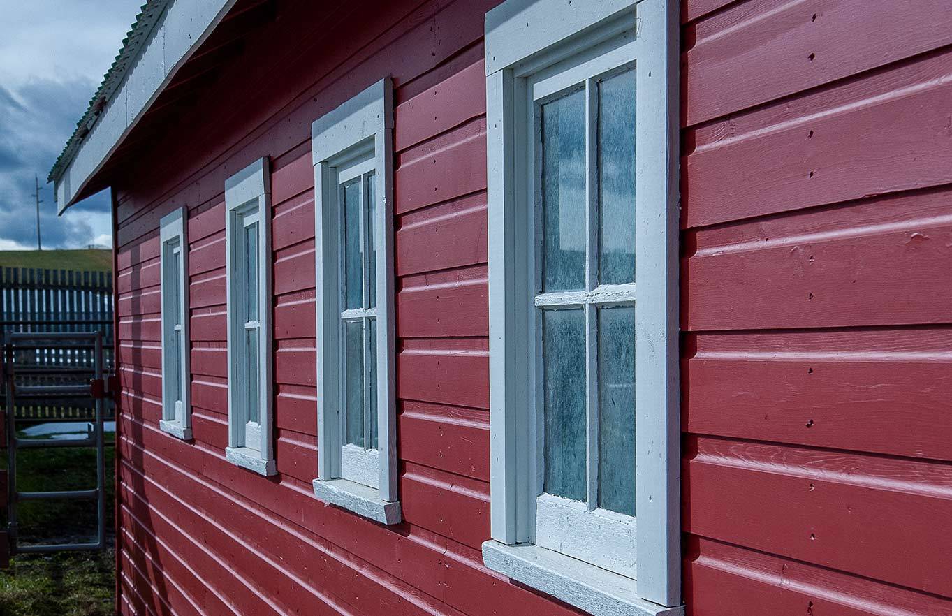 Close up of red home with four white windows showing cedar siding