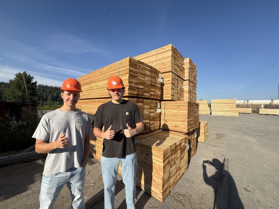 Two men in hard hats standing in a lumber yard with lumber in the background